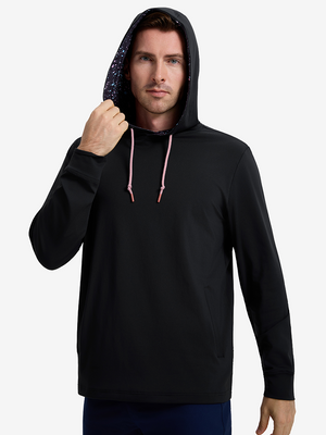 Front upper body shot of model wearing black soft stretchy hoodie with inner print hood and pulling the hood with one hand