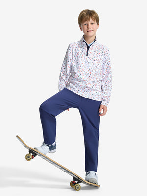 Front full body shot of model wearing white polka dots youth print midlayer Q-zip pullover sweatshirt standing casually on a skateboard