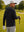 Back upper body angled shot of model wearing black soft stretchy hoodie with inner print hood, holding a golf ball in one hand and resting on a golf club with the other hand on the golf course