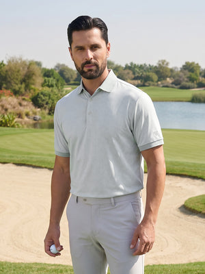 Front upper body shot of model wearing light grey moisture wicking jacquard golf shirt while holding a golf ball on the golf course