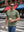 Front upper body angled shot of male model wearing green grey men's short sleeve slim fit Roma knit t-shirt, wearing sunglasses and holding a coffee cup on the street