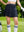 Front mid-length shot of female model wearing navy blue women's moisture-wicking athletic tennis skirt, one hand on waist and one gloved hand supporting a golf club
