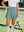 Front mid-length shot of female model wearing dusty blue  women's high waisted golf skirt with 4 inner pockets, left hand on waist and holding golf club in right hand on the  course